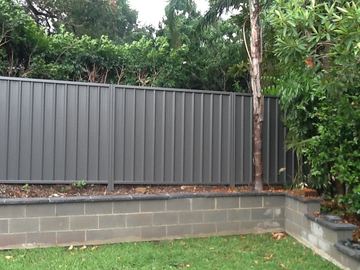 Charcoal Colorbond privacy fence standing on a concrete block retaining wall with garden plants in front