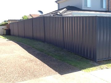 Long charcoal Colorbond privacy fence stretching across a gravel yard