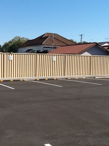 Cream Colorbond privacy fence running the length of a marked carpark
