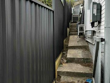 Charcoal Colorbond privacy fence running beside concrete steps at a white weatherboard house
