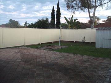 Cream Colorbond privacy fence enclosing a paved backyard