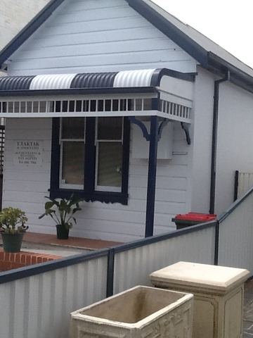 Cream Colorbond fence and pedestrian gate in front of a white weatherboard cottage with a striped verandah