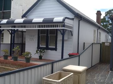 Cream Colorbond fence and pedestrian gate in front of a white weatherboard cottage with a striped verandah