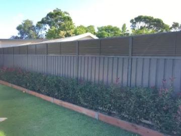 Mid grey Colorbond privacy fence running behind a clipped hedge on a lawn