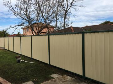 Cream Colorbond privacy fence spanning a suburban backyard with houses visible beyond