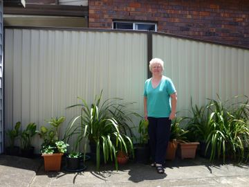 Cream Colorbond privacy fence beside potted garden plants with a person standing in front