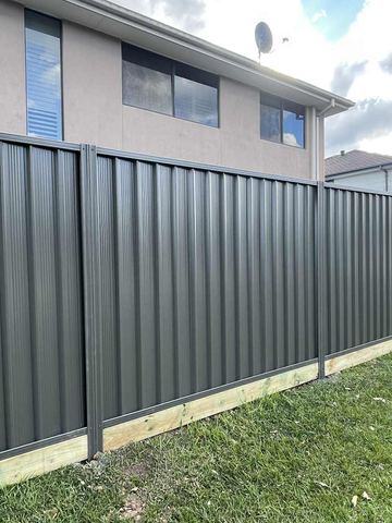 Long charcoal Colorbond privacy fence running across a lawn beside a white brick house
