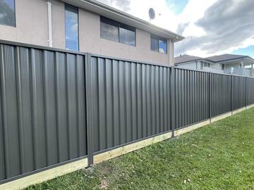 Long charcoal Colorbond privacy fence running across a lawn beside a white brick house