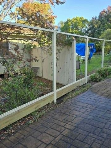 Open cream post-and-rail frames without infill curve along a brick patio and sleeper plinth in a leafy backyard.