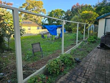 Empty cream frames on sleepers stand between a brick patio and lawn with a blue tarp over outdoor furniture.