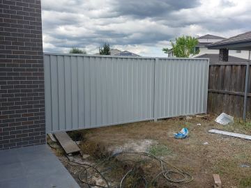 Installed Colorbond sheets sitting on a timber sleeper wall with a matching gate opening.