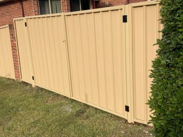 Installed sand Colorbond sheets sitting on a timber sleeper wall with a matching gate opening.