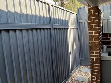 Mid grey Colorbond privacy fence returning to a brick house wall