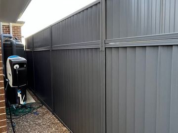 Charcoal panels with a mid-rail run beside a slimline tank, hose reel and pebble strip under house eaves.