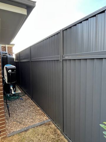 Charcoal panels with a mid-rail run beside a slimline tank, hose reel and pebble strip under house eaves.