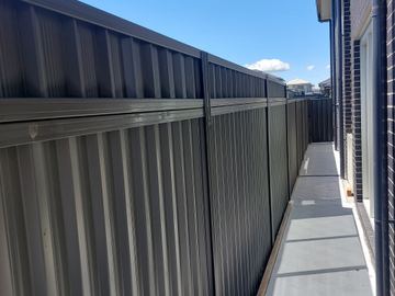 Charcoal panels with mid-rail and lattice top follow a long side path past dark brick and a distant slat gate.