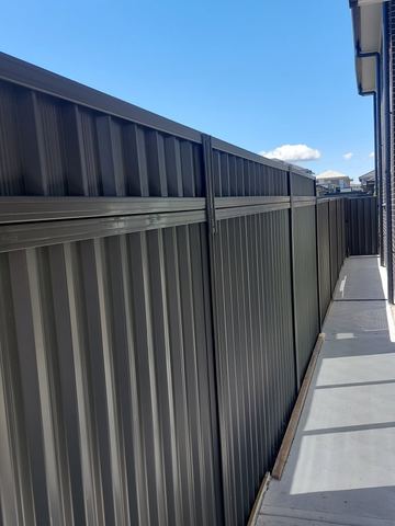 Charcoal panels with mid-rail and lattice top follow a long side path past dark brick and a distant slat gate.