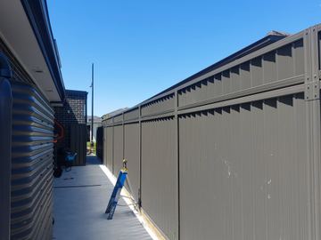 Charcoal Colorbond privacy fence along a paved courtyard path with a step stool