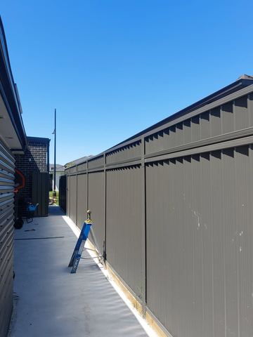 Charcoal Colorbond privacy fence along a paved courtyard path with a step stool
