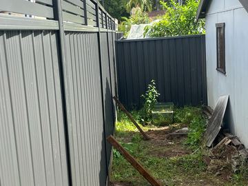 Charcoal panels with slat toppers and propped stakes stand beside a white garden shed on patchy side-yard soil.