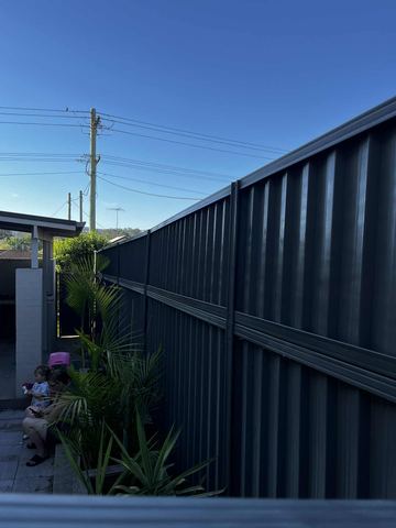 Charcoal panels stacked with a mid-rail run beside pavers and palms with people sitting on a ledge in the background.
