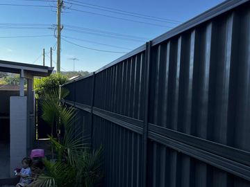 Charcoal panels stacked with a mid-rail run beside pavers and palms with people sitting on a ledge in the background.