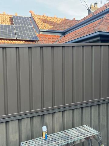 Charcoal lower panels with basalt upper sheets include a narrow ribbed gate beside a terracotta roof with solar panels.