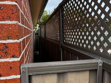 Bronze panels with diamond lattice fill a tight side path beside red brick with palms above the roofline.