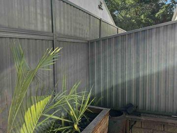 Mid grey Colorbond privacy fence turning a corner beside a potted plant