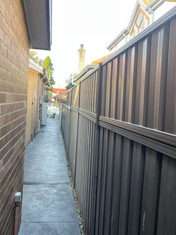 Dark bronze corrugated panels with a mid-rail line a textured concrete side path between brick houses.