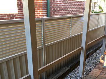 Cream Colorbond fence with a slat topper seen under a pergola post