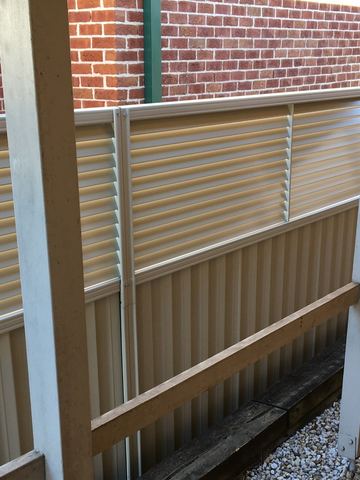 Cream Colorbond fence with a slat topper seen under a pergola post