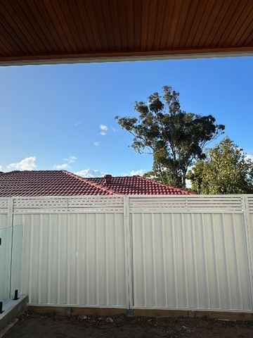 White Colorbond privacy fence standing beside a frameless glass pool barrier