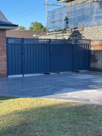 Charcoal panels with diamond lattice and a wide double gate open over fresh concrete near scaffolding.