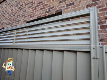 Cream Colorbond fence with a white slat topper bolted against a brick house wall