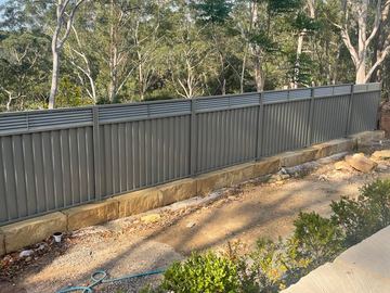 Mid grey Colorbond privacy fence on a sandstone plinth along a bushland boundary
