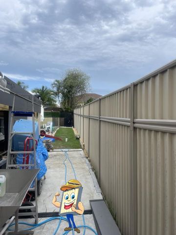 Cream Colorbond privacy fence along a concrete backyard path with an installer at work