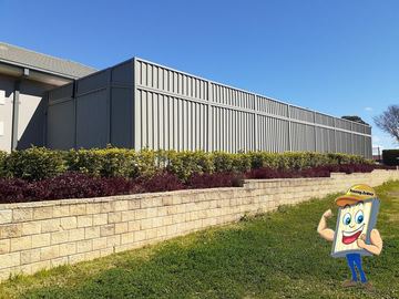 Charcoal Colorbond privacy fence behind a clipped hedge on a concrete block retaining wall