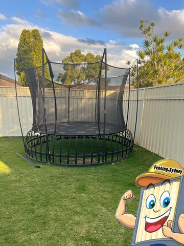 Cream panels wrap a lawn corner behind a large trampoline with suburban trees and sky above.