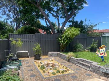 Charcoal Colorbond privacy fence enclosing a gravel courtyard with a small garden bed