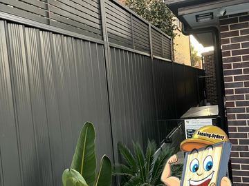 Charcoal Colorbond fence with a slat topper returning against a brick house wall