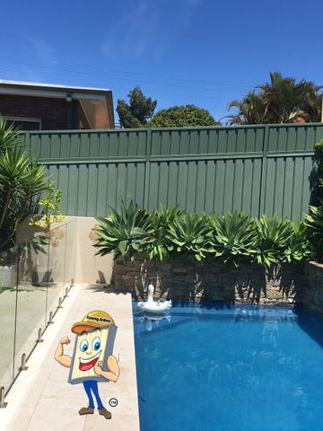 Cream Colorbond privacy fence beside a glass pool fence and tropical plants