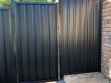 Charcoal panels and a gate step up beside a brown brick patio propped with timber during installation.