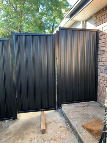 Charcoal panels and a gate step up beside a brown brick patio propped with timber during installation.