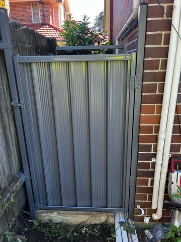 Mid grey Colorbond pedestrian gate hung against a brick house wall