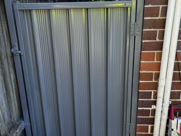 Mid grey Colorbond pedestrian gate hung against a brick house wall