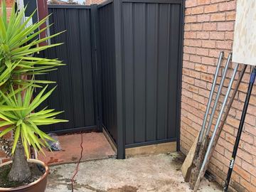 Charcoal Colorbond pedestrian gate set in a brick alcove beside a potted plant