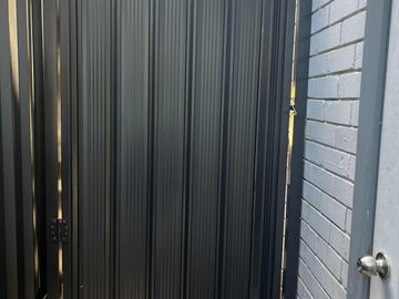 Close view of a charcoal Colorbond pedestrian gate hard against painted brick