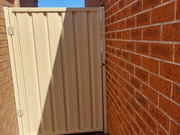Cream gate catches sunlight on white pebbles between contrasting brick walls in a narrow side return.