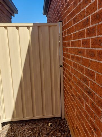 Cream gate catches sunlight on white pebbles between contrasting brick walls in a narrow side return.